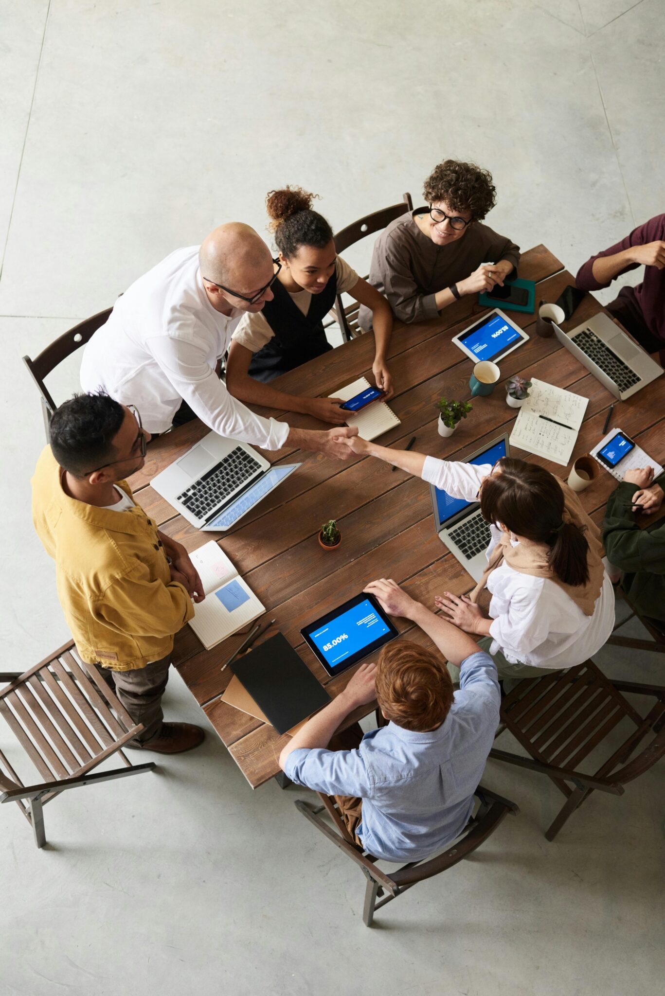 Diverse business team shaking hands over a meeting table with laptops and charts